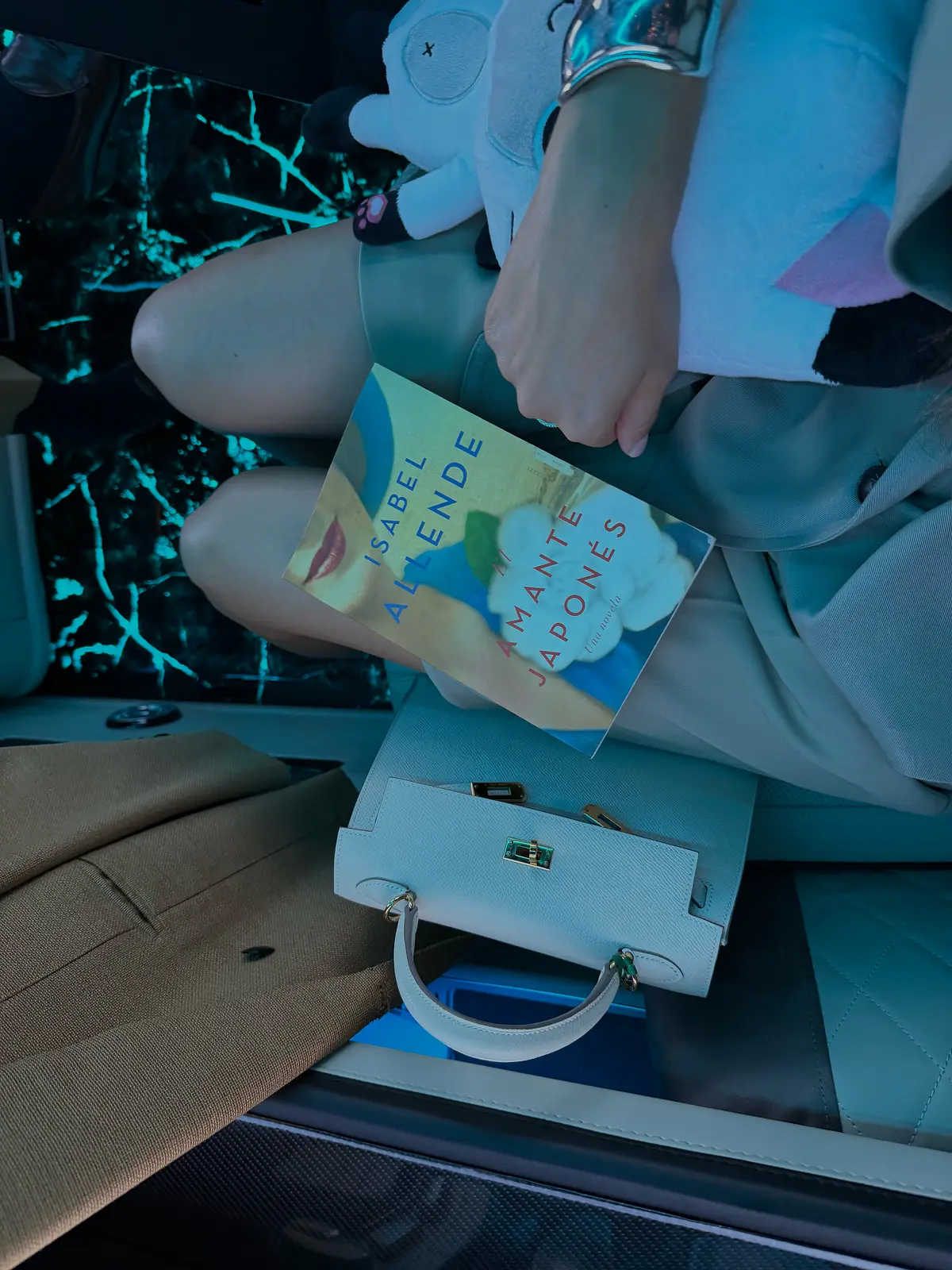 A copy of Isabel Allende’s El amante japonés resting on a lap beside a white handbag.