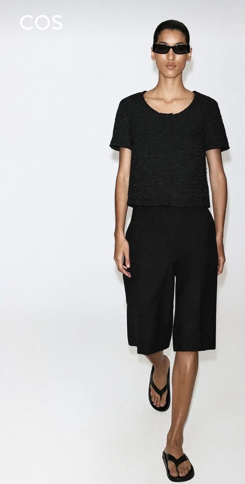 Model wearing black COS Bermuda shorts with a black top.