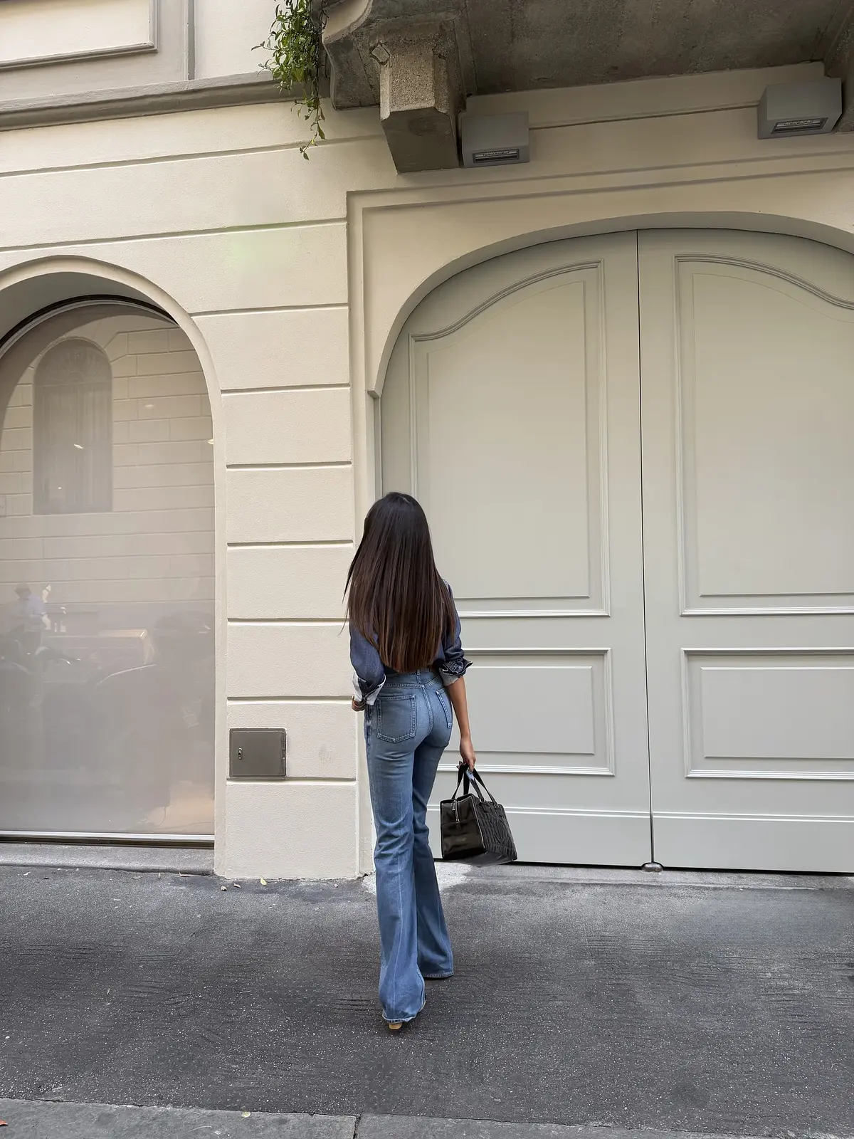 Il look di Sharon visto da dietro, con camicia in denim, jeans e borsa nera in mano.