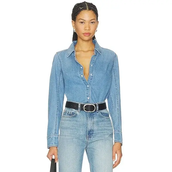 Modella con camicia aderente in denim blu, jeans e cintura nera.