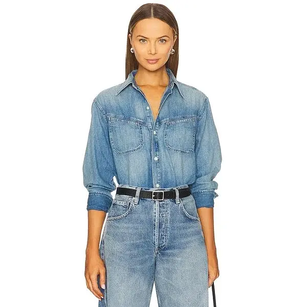 Modella con camicia in denim blu con tasche sul petto e maniche arrotolate.