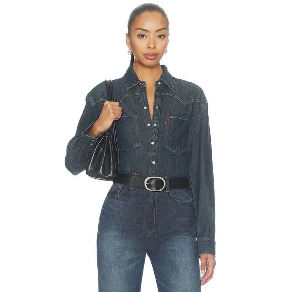 Modella con camicia western in denim scuro e borsa nera a spalla.