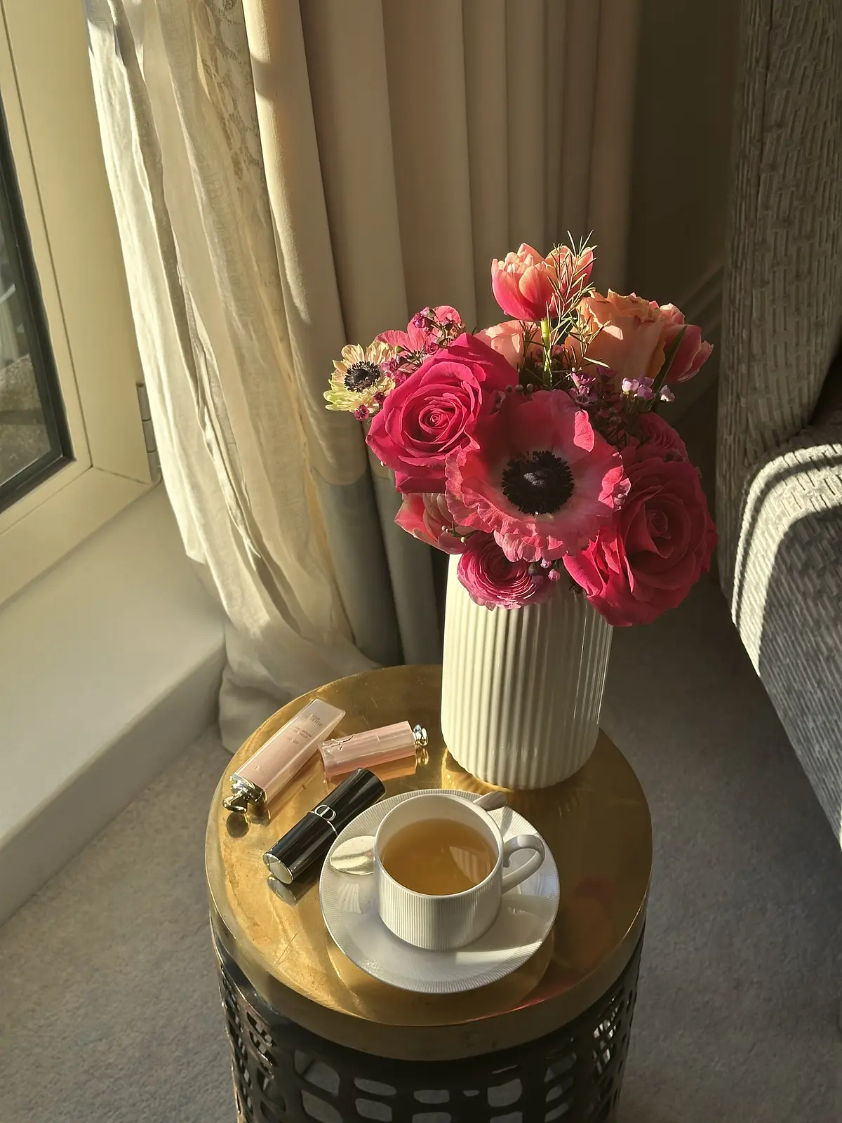 Fiori rosa, una tazza di tè e cosmetici su un tavolino accanto alla finestra.